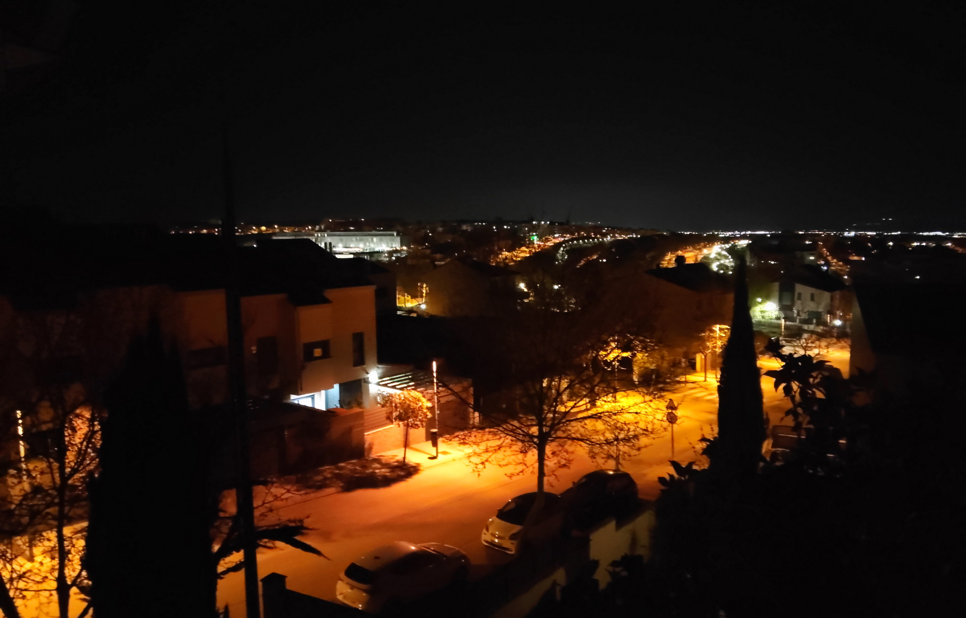 Vista nocturna de una ciudad iluminada, con calles y casas, bajo un cielo estrellado.