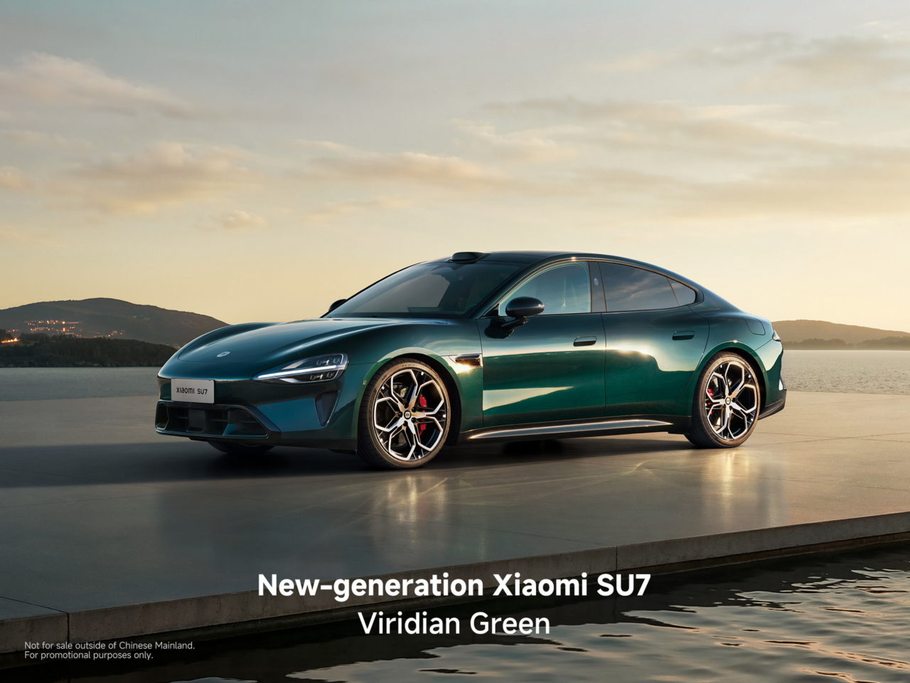 Coche Xiaomi SU7 en color verde esmeralda sobre plataforma junto al mar, con paisaje montañoso al fondo.