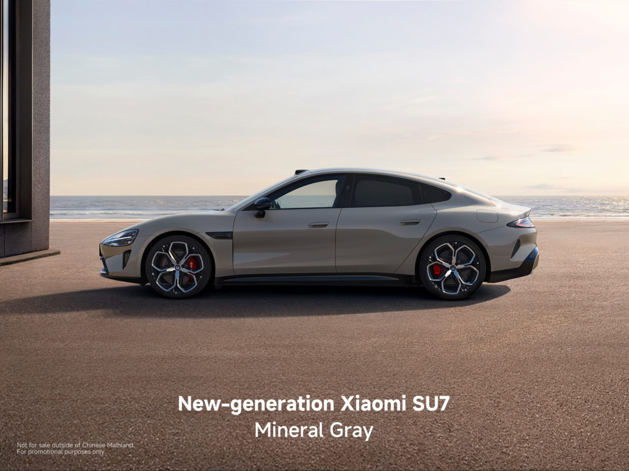 Coche Xiaomi SU7 gris mineral de nueva generación estacionado junto al mar al atardecer.