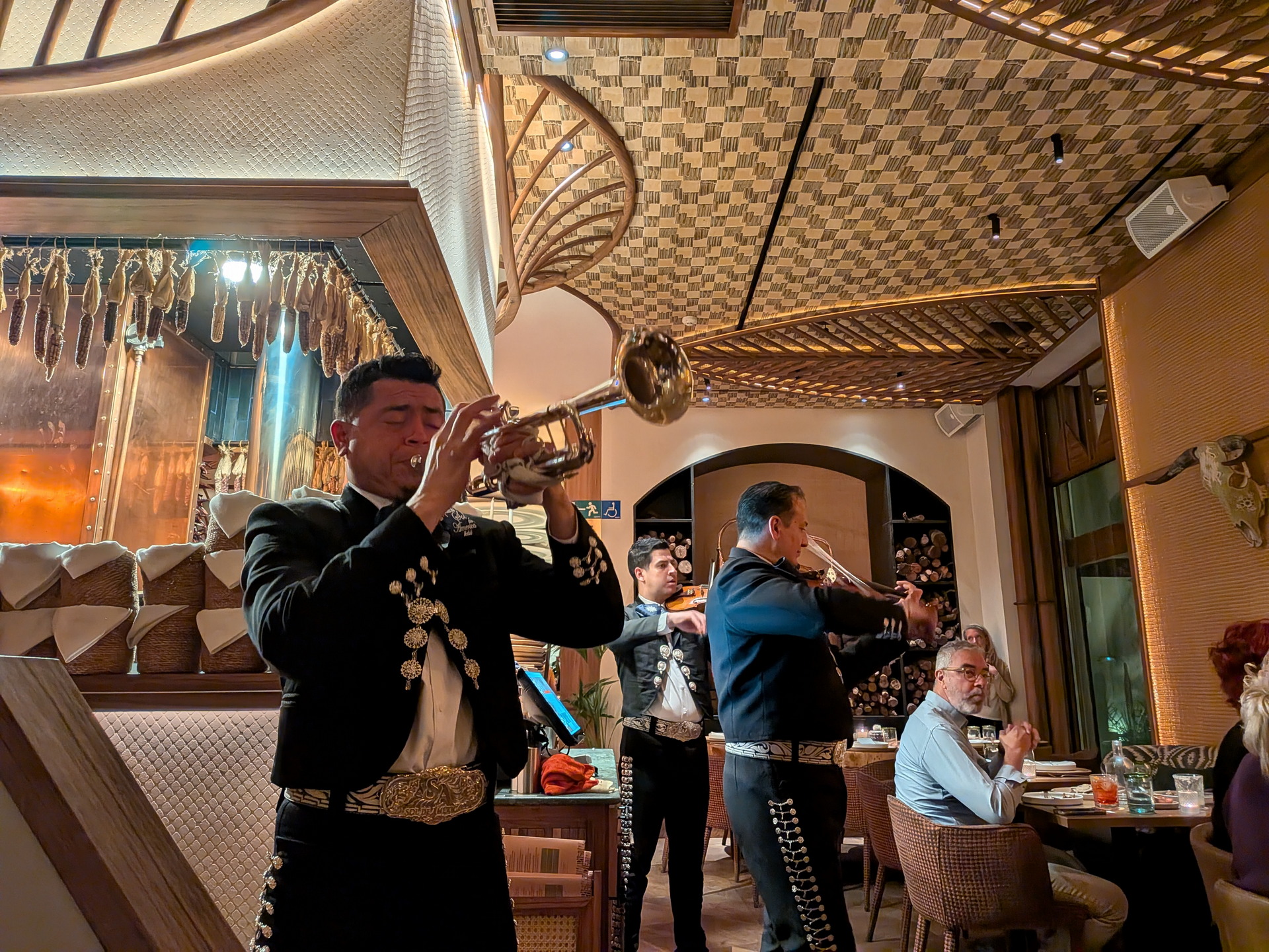 Mariachi tocando trompeta y violines en un restaurante elegante, ambientando la noche con música tradicional mexicana.