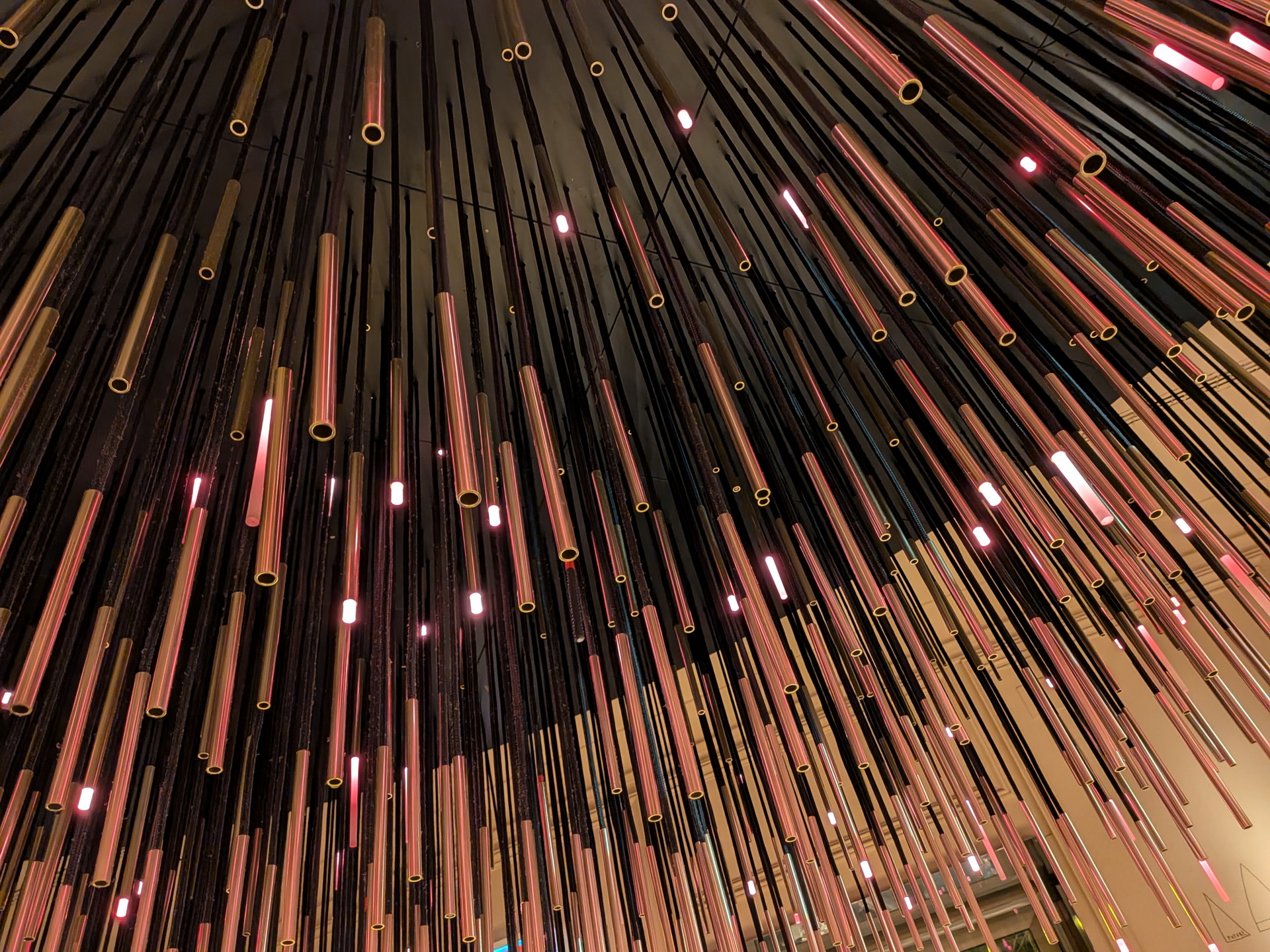 Techo decorado con tubos colgantes iluminados en tonos rosados y dorados, creando un efecto visual moderno.