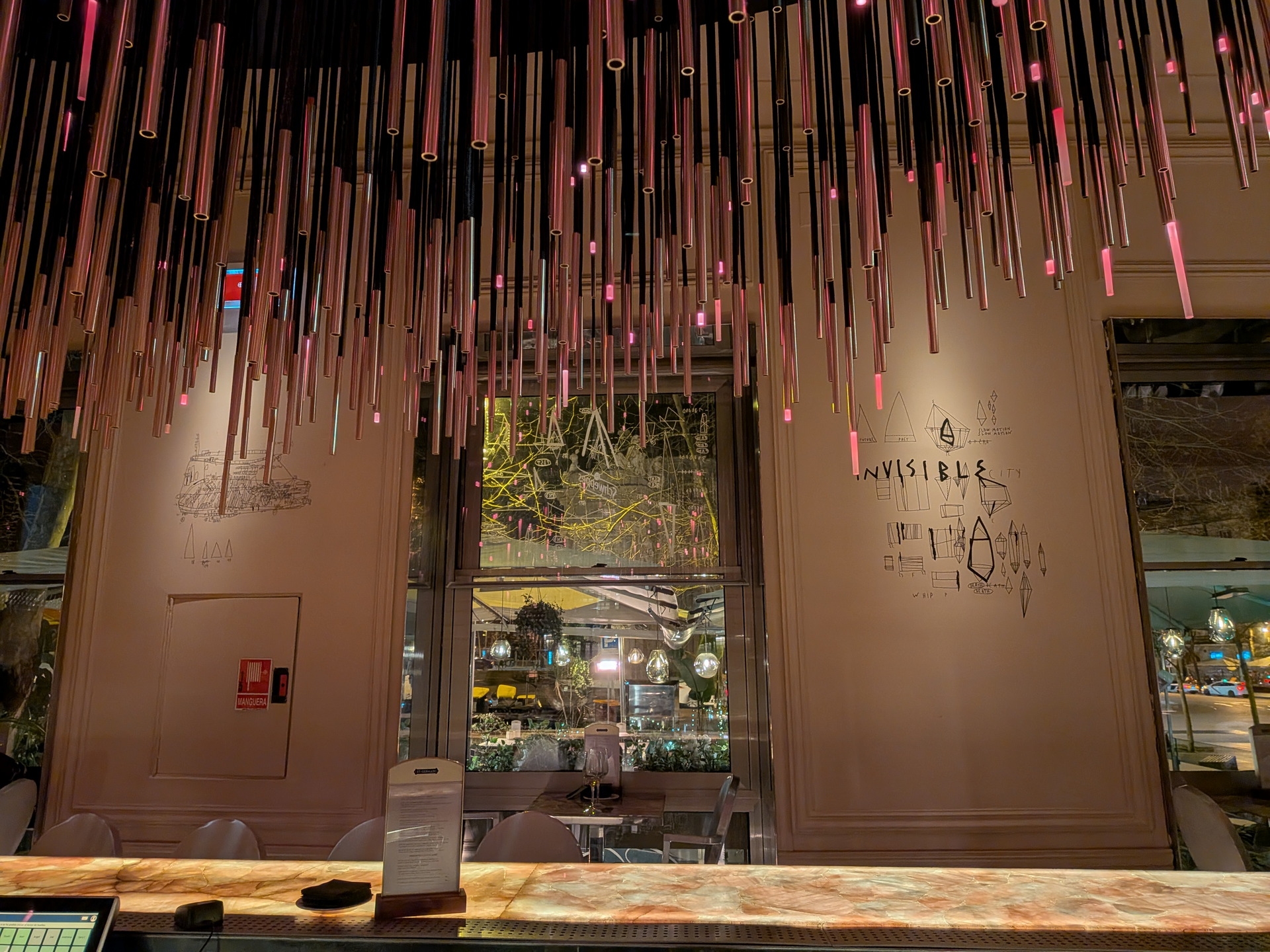 Bar moderno con techo de tubos colgantes y murales en las paredes. Ambiente iluminado y elegante.