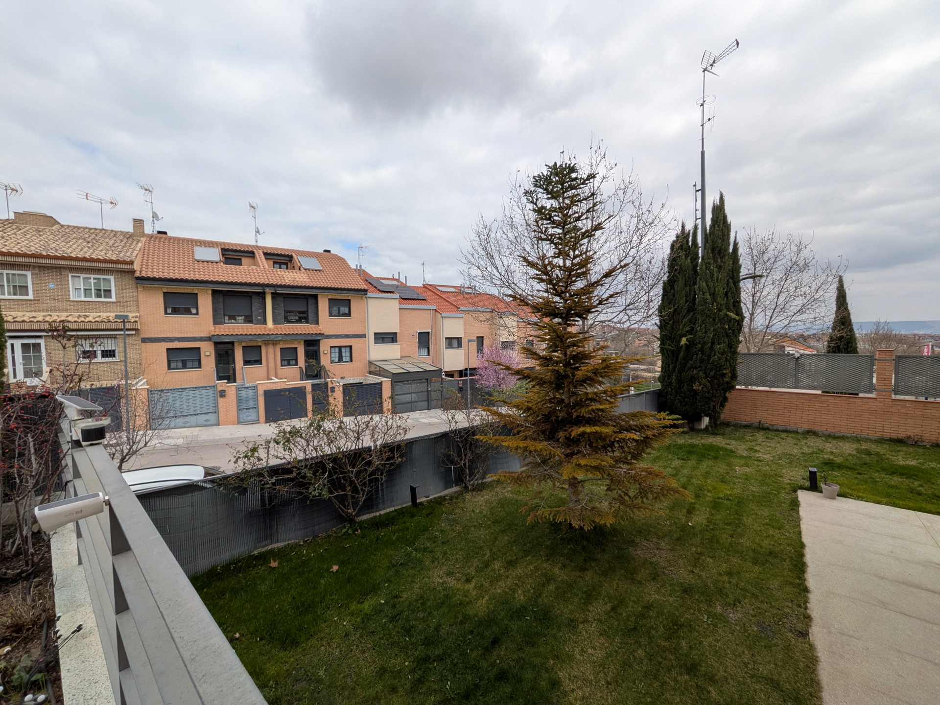 Vista de un vecindario residencial con casas adosadas y un jardín con árboles en un día nublado.