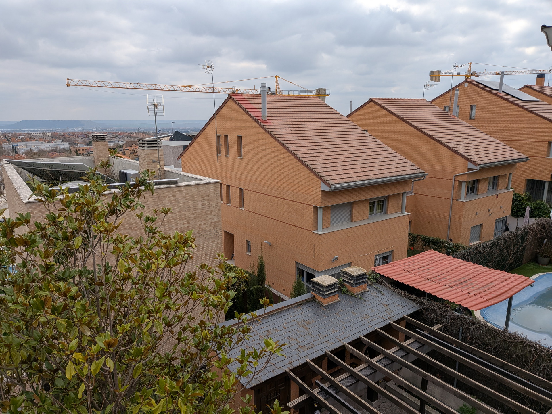 Vista de casas modernas de ladrillo con techos inclinados, rodeadas de grúas en construcción y vegetación.