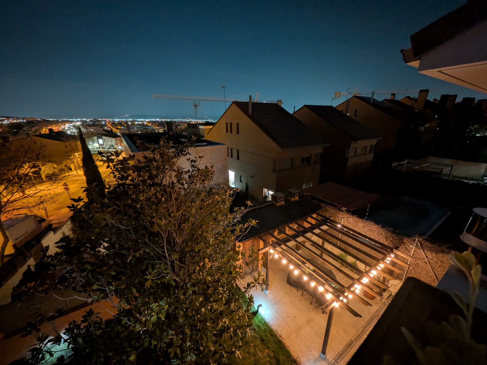 Vista nocturna de un vecindario con luces resplandecientes sobre una terraza y cielos despejados en el horizonte.