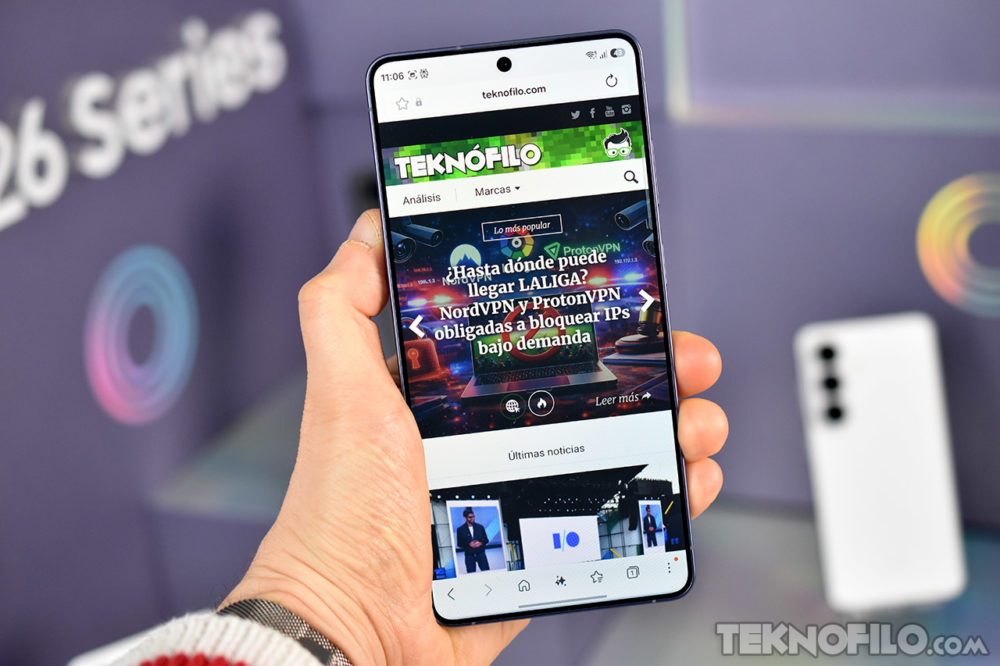 La serie Galaxy S26 no mejora la fatiga visual para los usuarios sensibles al parpadeo Persona sosteniendo un smartphone con la página web de Teknofilo en pantalla, mostrando noticias tecnológicas.