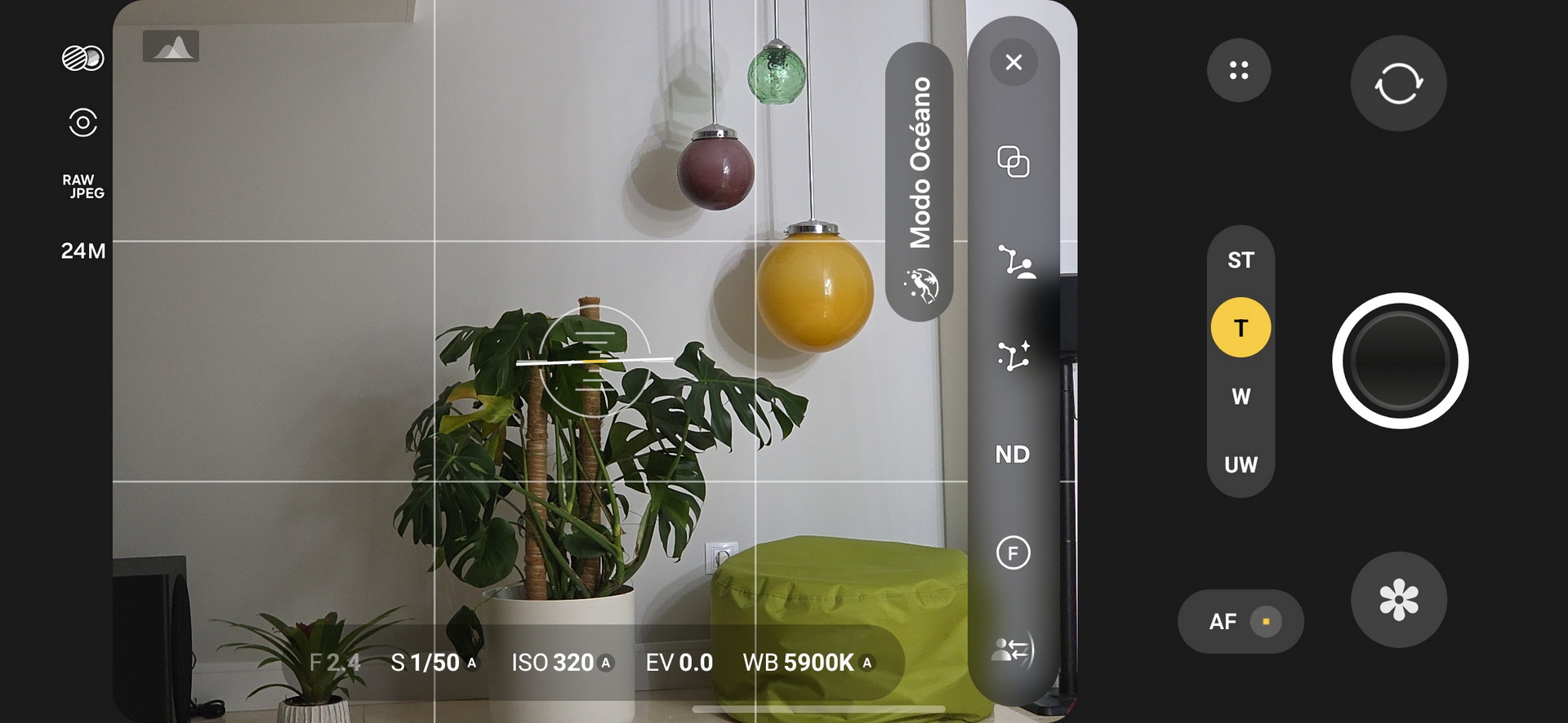 Cámara de smartphone enfocando lámparas colgantes de colores y una planta en maceta junto a un cojín verde.