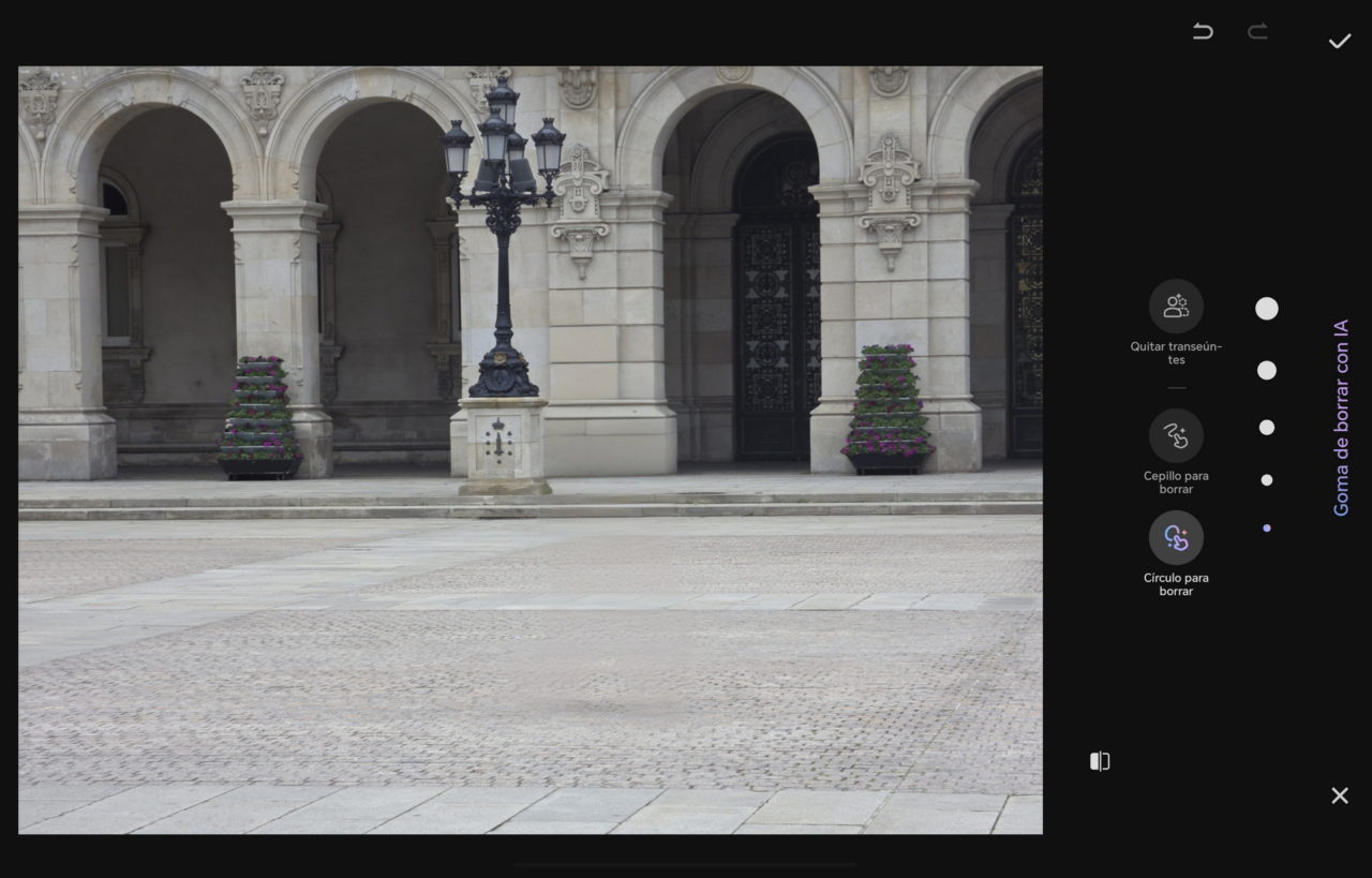 Antigua fachada de piedra con arcos, farola negra y flores moradas en el centro histórico de una ciudad.