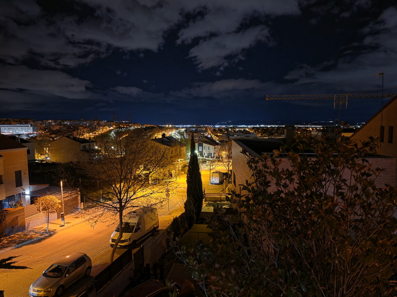 Vista nocturna de una ciudad iluminada, con cielo nublado y calles iluminadas por luces amarillas.