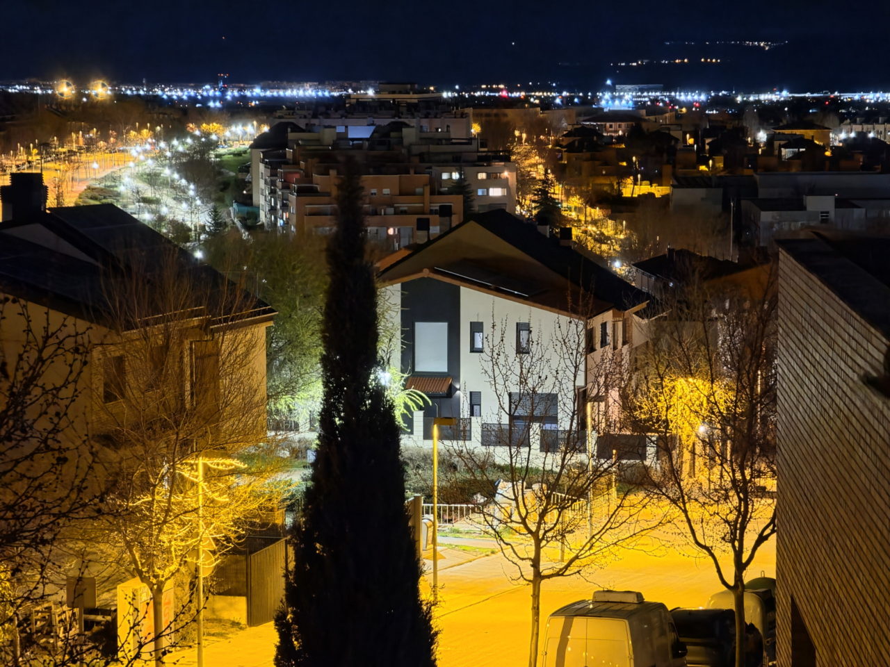 Vista nocturna urbana, luces de calle iluminan las casas y árboles en un barrio residencial tranquilo.