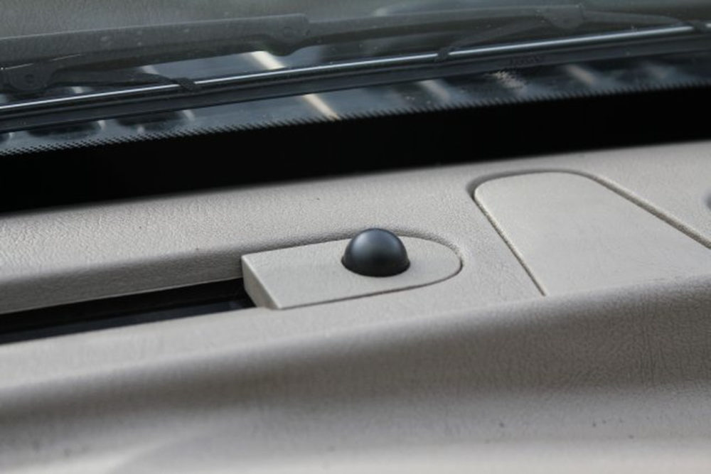 El misterioso círculo del salpicadero: esto es lo que hace realmente en tu coche Botón en salpicadero de automóvil junto al parabrisas, con acabado en color claro y diseño minimalista.