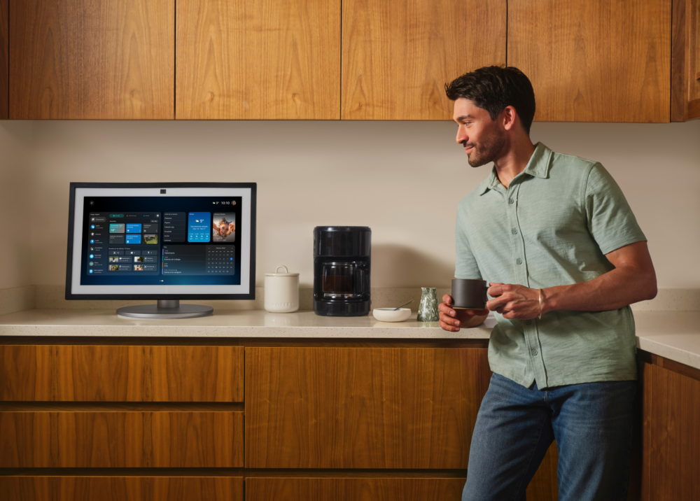Hombre en cocina moderna viendo pantalla inteligente, sosteniendo taza de café. Tecnología y confort hogareño.