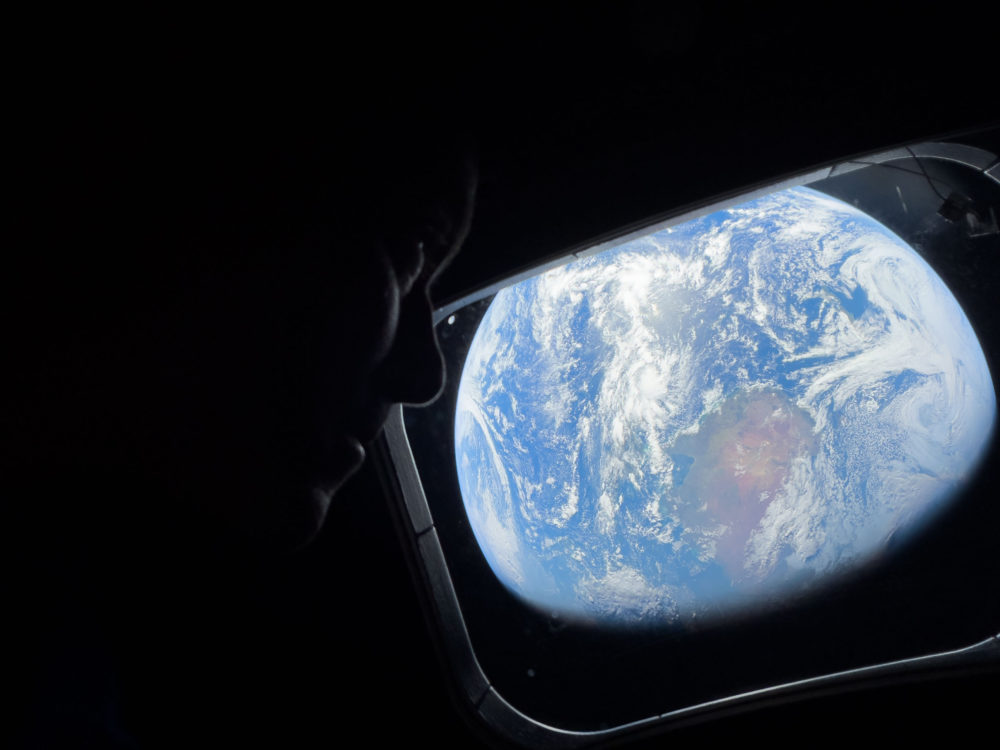 Astronauta mirando la Tierra desde el espacio a través de una ventana de la nave espacial, vista impresionante del planeta.