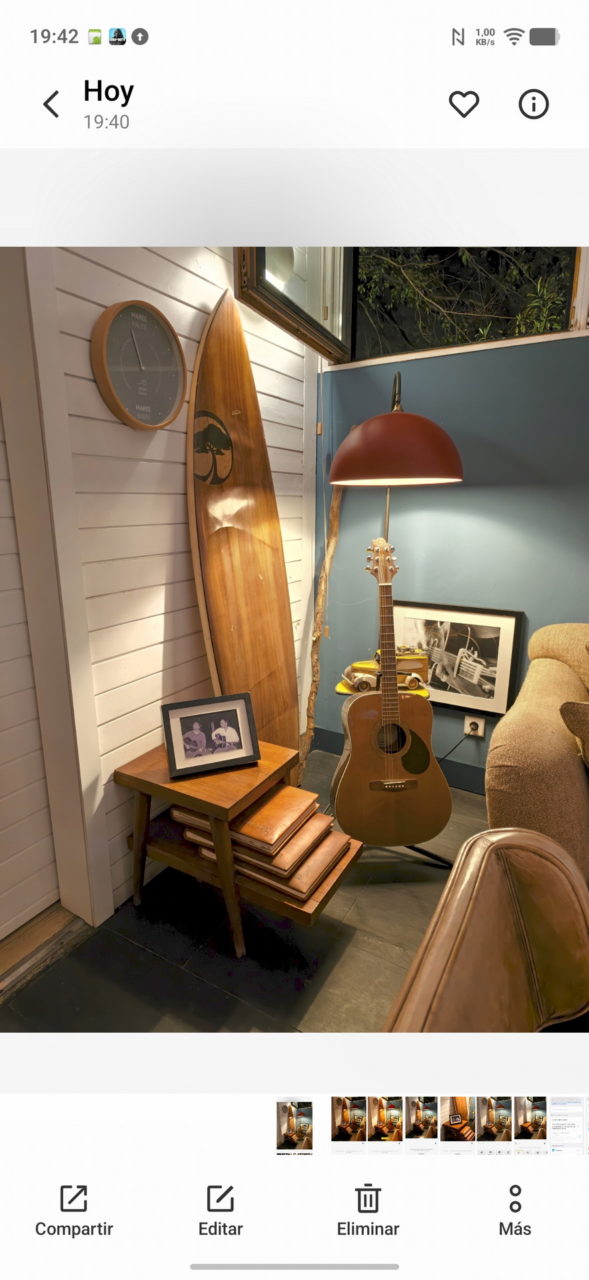 Esquina acogedora con guitarra, lámpara, tabla de surf y mesa de madera junto a sillón y cuadro.