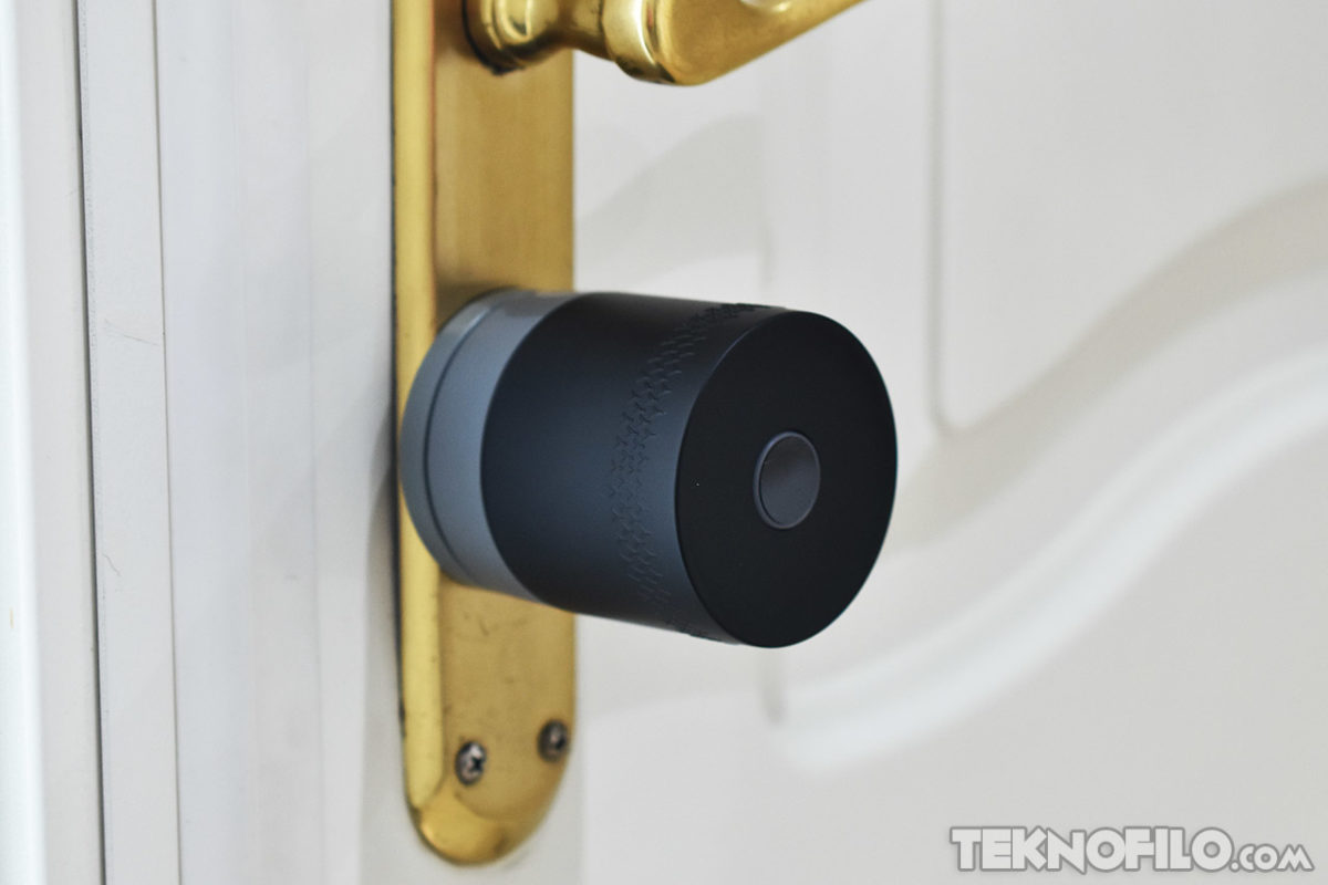 Cerradura inteligente negra instalada en puerta blanca con manilla dorada, innovador dispositivo de seguridad doméstica.