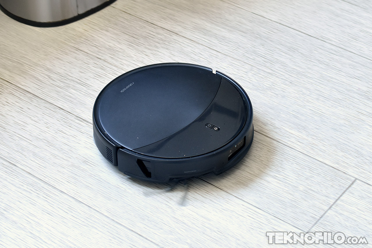 Aspiradora robot negra sobre suelo de madera, dispositivo inteligente para limpieza automática del hogar.