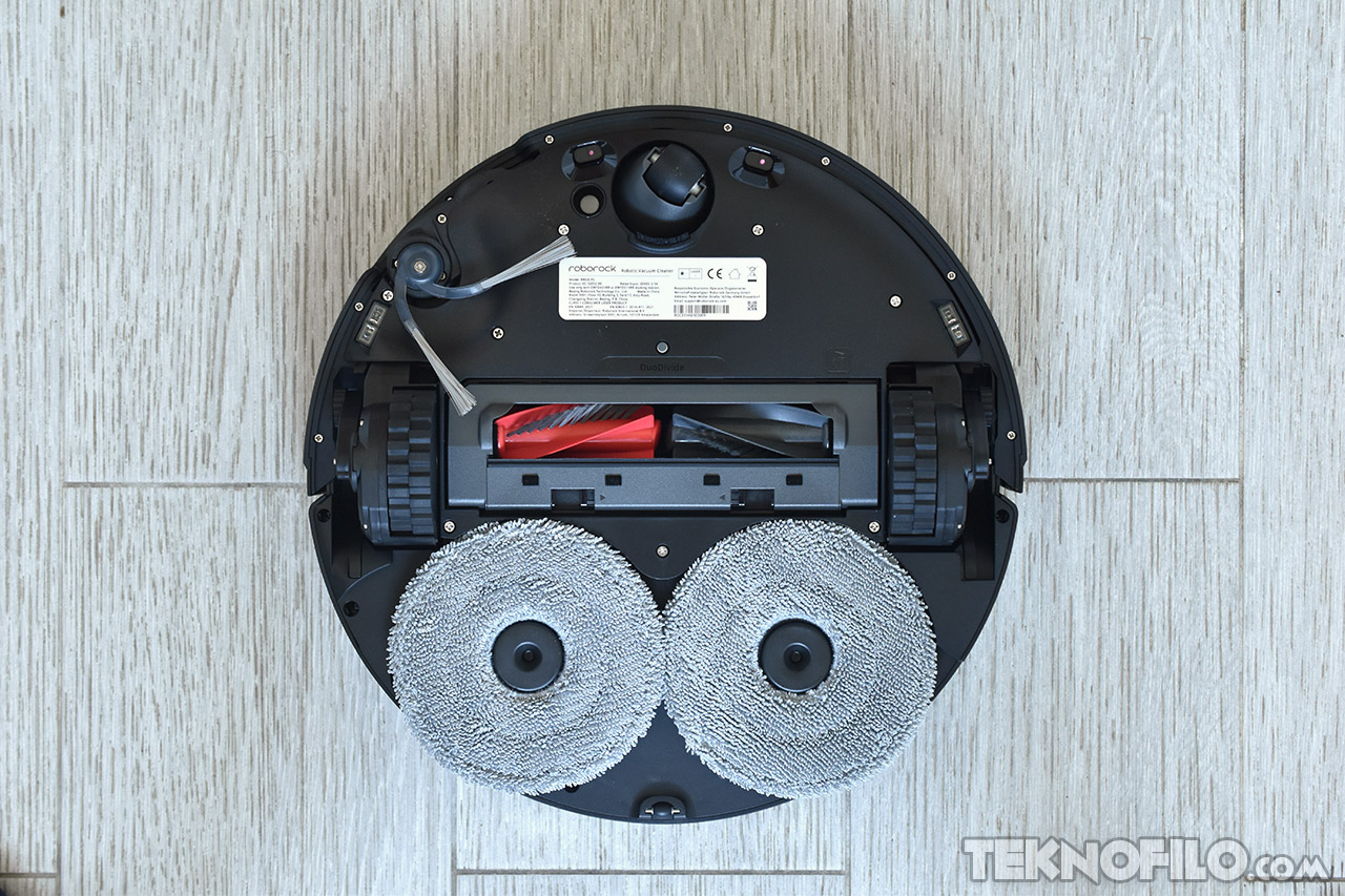 Parte inferior de un robot aspirador avanzado con cepillos rotativos sobre suelo claro.