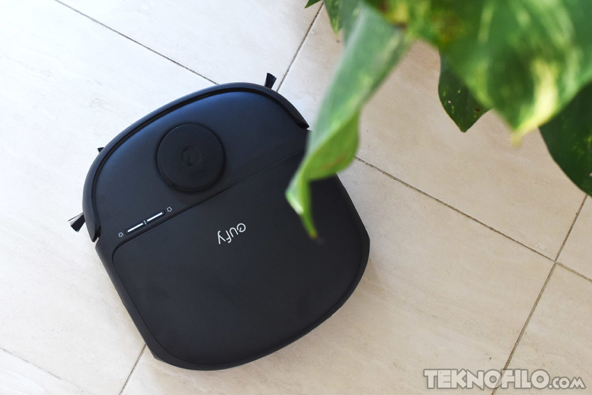 Robot aspirador en piso claro junto a una planta verde. Tecnología de limpieza eficiente.