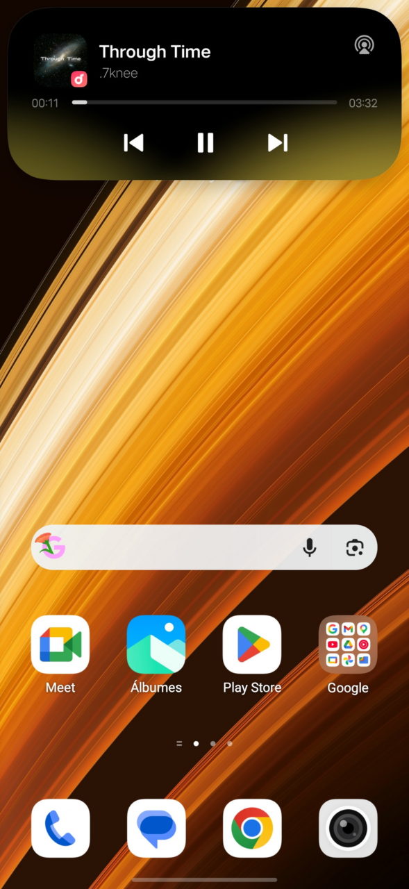 Pantalla de inicio de Android con fondo naranja y widget musical reproducido, mostrando iconos de apps populares.