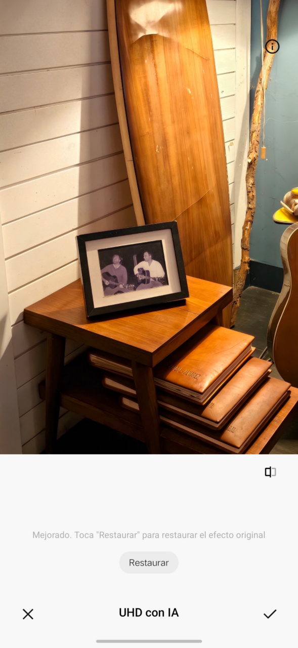 Mesa de madera con portarretratos y carpetas de cuero, tabla y guitarra decorando una pared blanca.