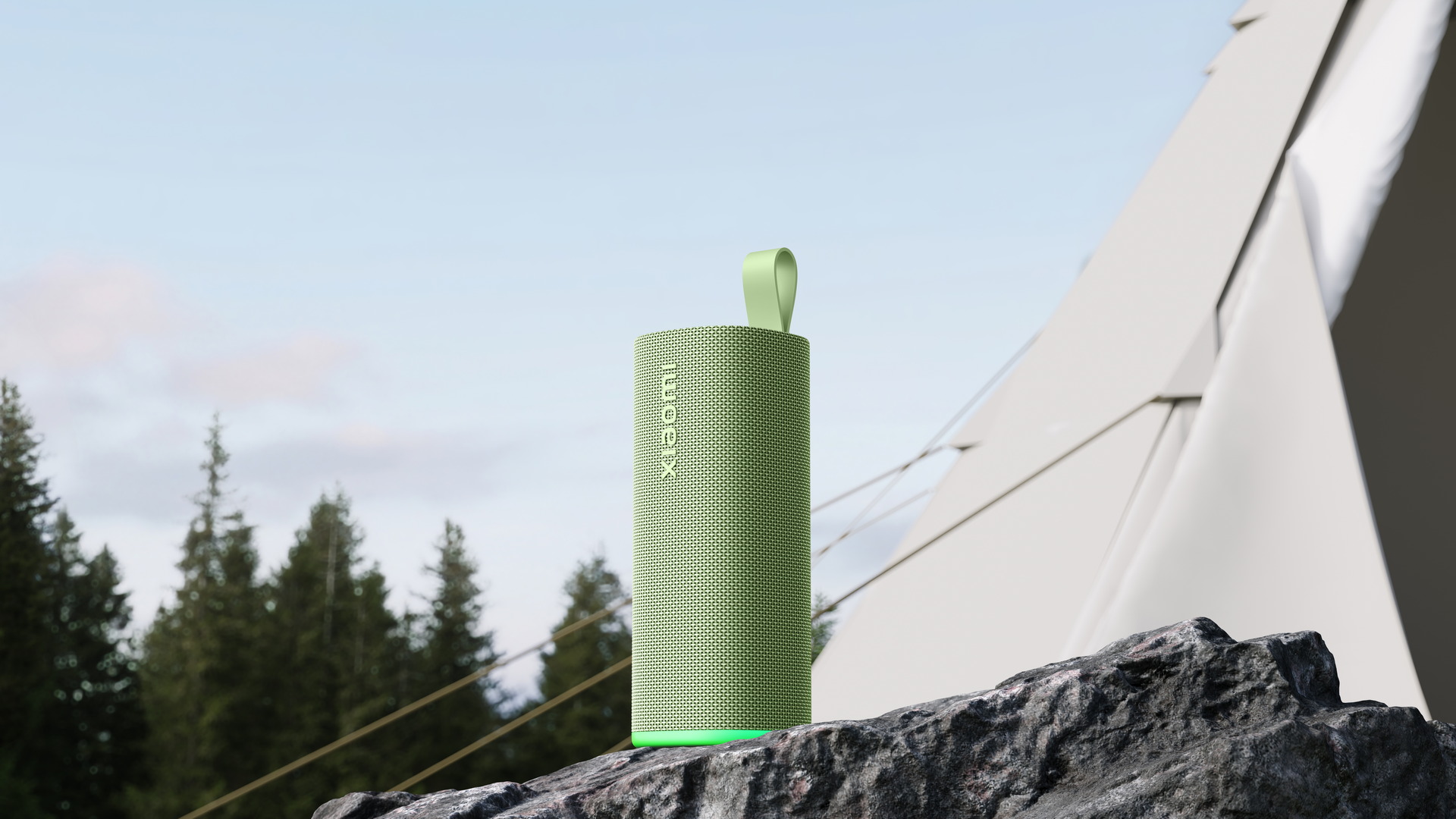 Alt text: Altavoz portátil verde sobre roca con fondo de bosque y cielo azul, ideal para exteriores.