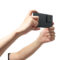 Manos sosteniendo smartphone negro, con cámara de triple lente, para fotografía o video, fondo blanco.