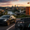 Tesla lleva su conducción autónoma supervisada a dos países europeos Coche eléctrico negro Tesla en carretera con vista de ciudad al atardecer y castillo en colina, bandera ondeando.