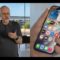 Usuario revisa un iPhone con íconos de aplicaciones visibles en primer plano, en un entorno moderno y luminoso.