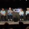 Personas en panel de discusión en conferencia tecnológica con fondo de logotipo WWDC, cuatro hombres sentados hablando.
