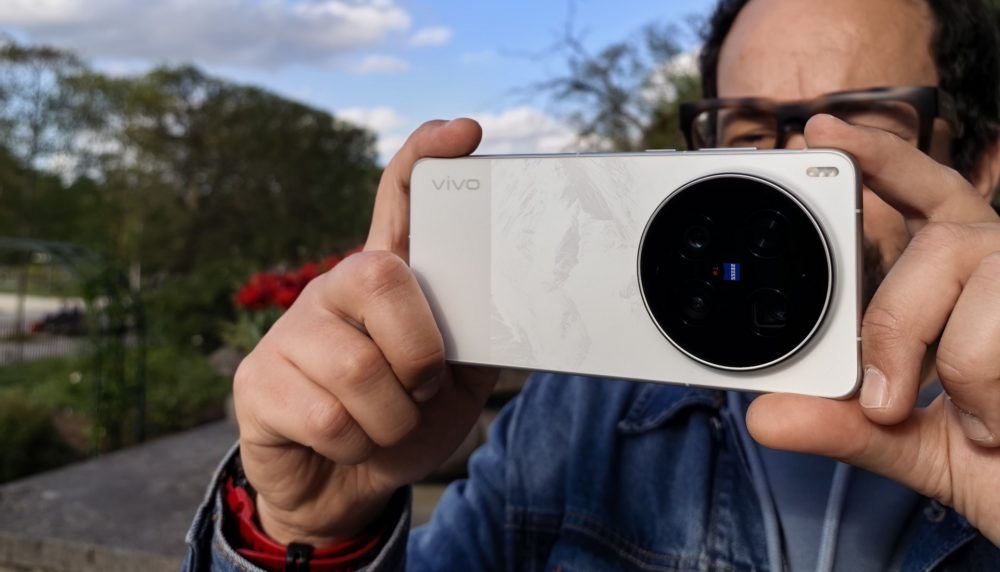 Persona usando un teléfono Vivo para fotografiar, destacando cámara Zeiss en un ambiente al aire libre.