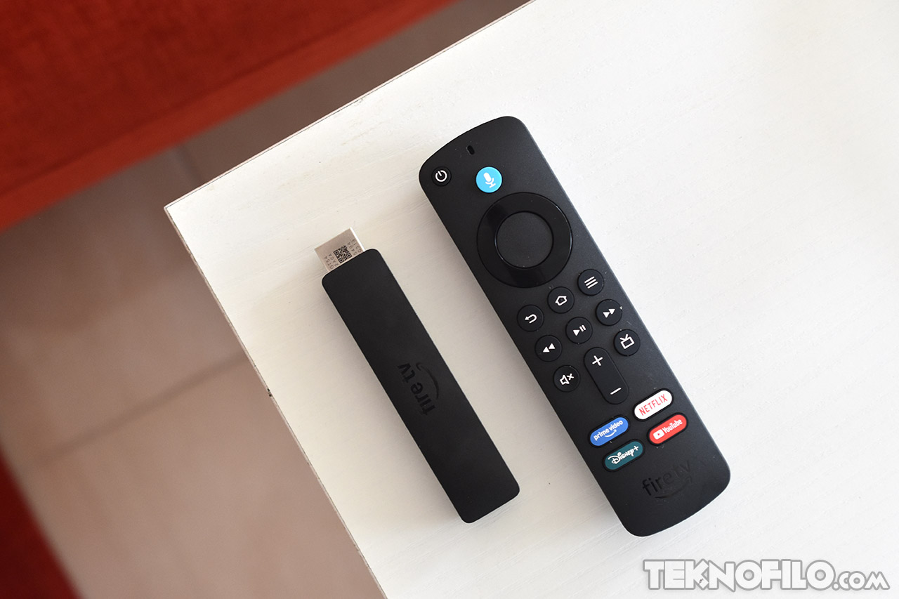 Control remoto de Fire TV Stick con botones de acceso rápido a Netflix, YouTube y más, sobre mesa blanca.