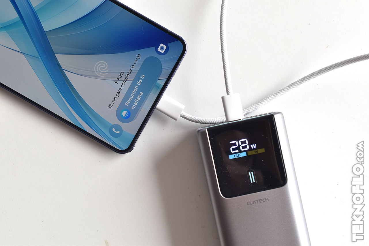 Carga rápida de móvil conectado a un cargador portátil mostrando 28W de salida. Pantalla del teléfono al 50% de carga.