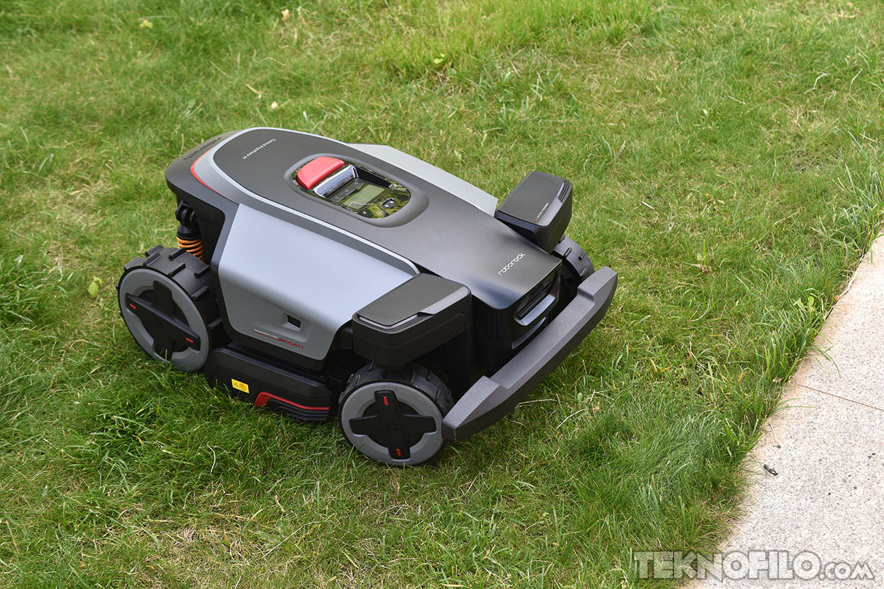 Cortacésped robot en césped verde junto a acera, tecnología avanzada de jardinería automatizada.