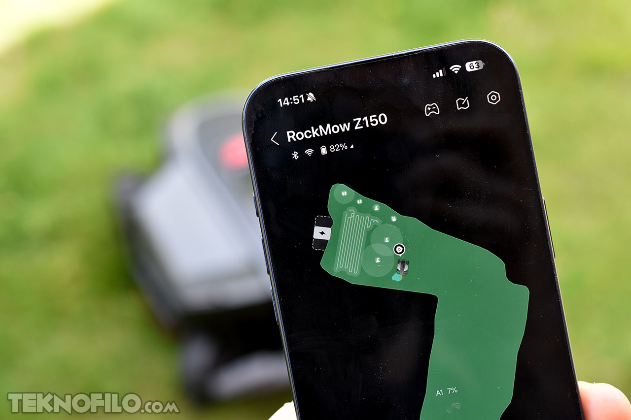 Aplicación móvil controlando robot cortacésped RockMow Z150 en pantalla de smartphone sobre césped verde.