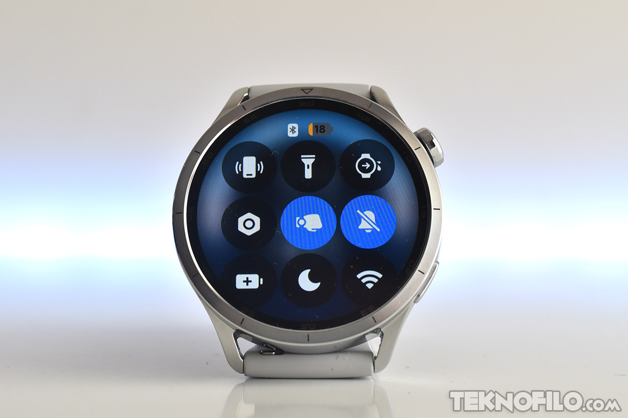 Reloj inteligente plateado con interfaz de control de aplicaciones en pantalla circular iluminada.