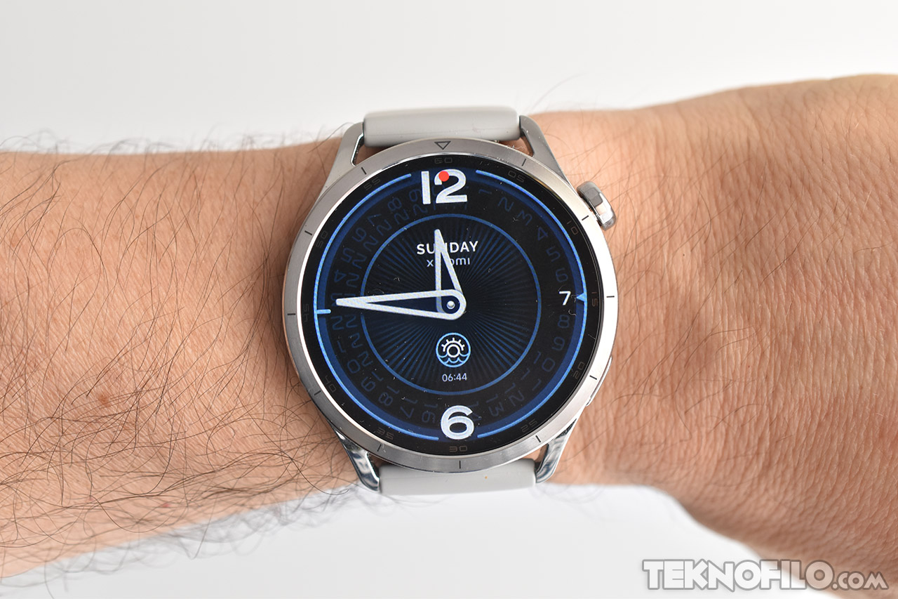 Reloj inteligente con esfera digital iluminada y correa blanca, en la muñeca de una persona. Hora mostrada: 06:44.