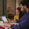 Nuevas cuentas infantiles de Apple: más control sobre apps, webs, mensajes y horarios Padre e hija usando tableta en sala moderna, aprendiendo juntos. Frutas y vaso en la mesa completan la escena acogedora.