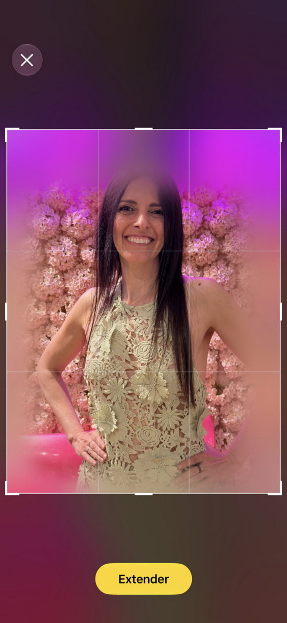 Una mujer sonriente con vestido floral frente a un fondo de flores rosas.