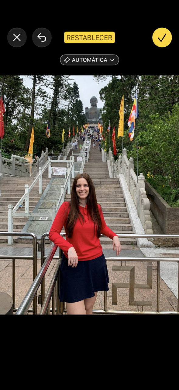 Mujer sonriendo frente al Gran Buda de Tian Tan en Hong Kong, rodeada de banderas y escaleras.