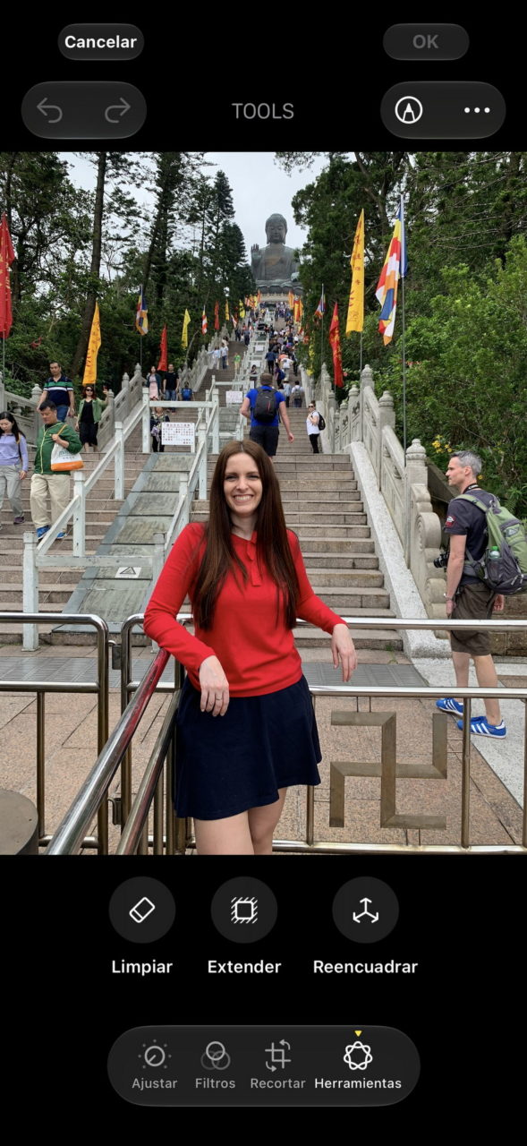 Mujer sonriendo frente a la escalera que lleva al Gran Buda, rodeada de banderas y vegetación.