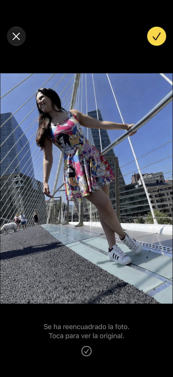 Mujer con vestido colorido y zapatillas blancas en un puente moderno bajo un cielo azul claro en la ciudad.