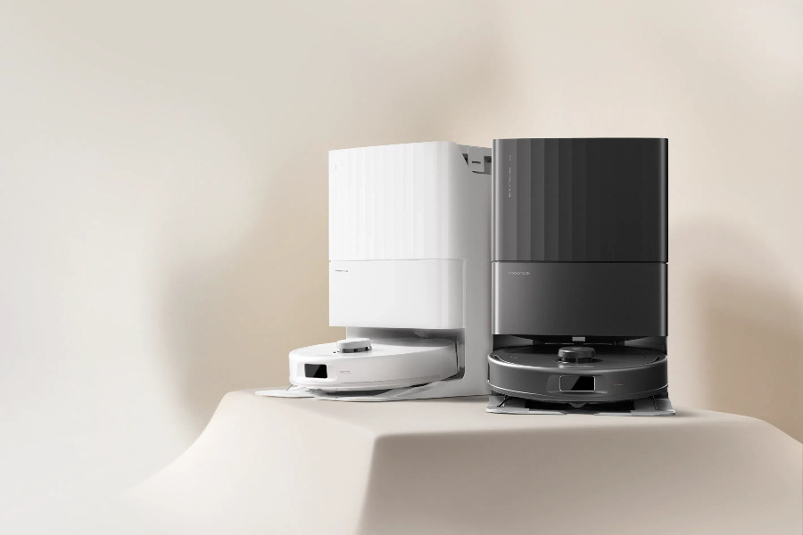 Dos robots aspiradores, uno blanco y otro negro, sobre una superficie beige para limpieza automática del hogar.