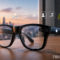 Gafas inteligentes en una mesa con íconos holográficos de navegación, cámara y música; vista de ciudad al atardecer.
