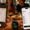 Personas dividiendo cuenta de restaurante con smartphones en mesa, usando aplicación para escanear y gestionar pagos.