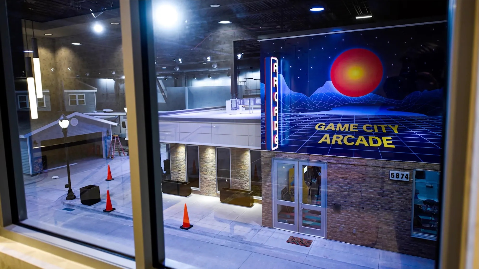 Fachada de Game City Arcade con letrero retro iluminado y calle vacía por la noche vista desde una ventana.