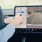 Tesla prepara una gran mejora para que sus coches aparquen donde tú quieres Conductor interactuando con pantalla táctil de auto eléctrico mostrando cámara trasera y controles de navegación.