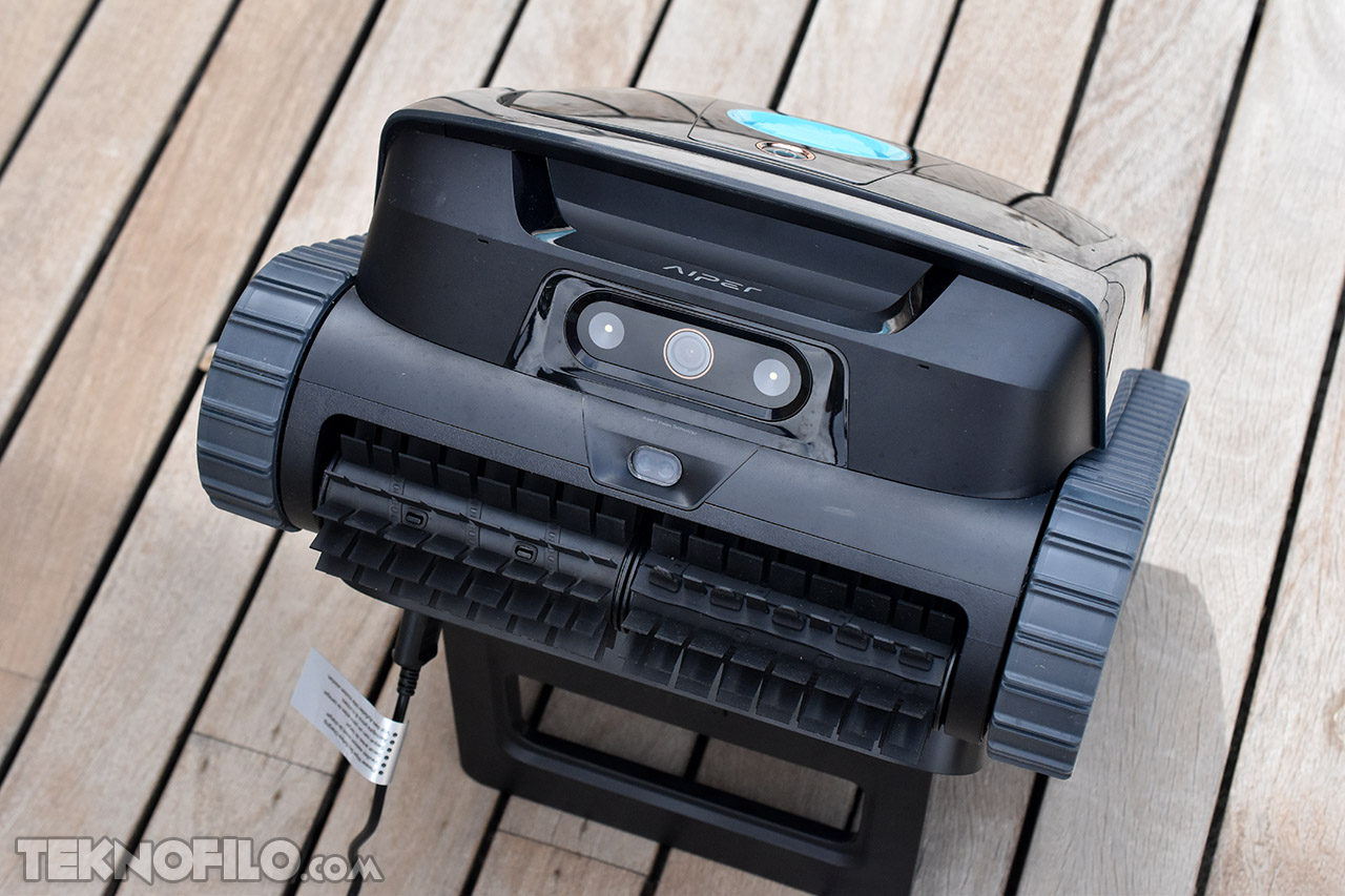 Robot limpiador de piscinas negro sobre suelo de madera, diseño moderno y compacto.