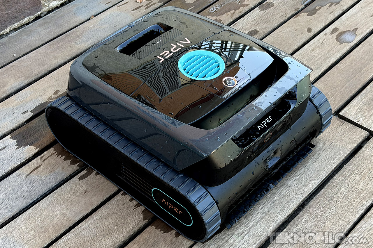 Robot limpiador de piscinas sobre suelo de madera mojada, diseño moderno en negro y azul.