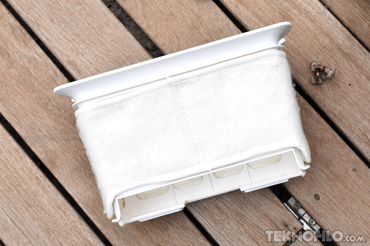 Caja blanca con funda de tela blanca sobre una superficie de madera, vista desde arriba.