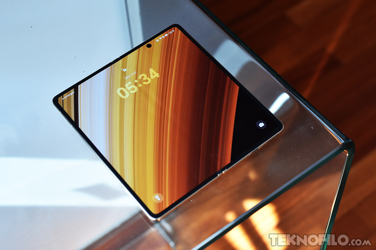 Pantalla de smartphone plegable display AMOLED encendido sobre mesa de vidrio, mostrando hora 05:34.